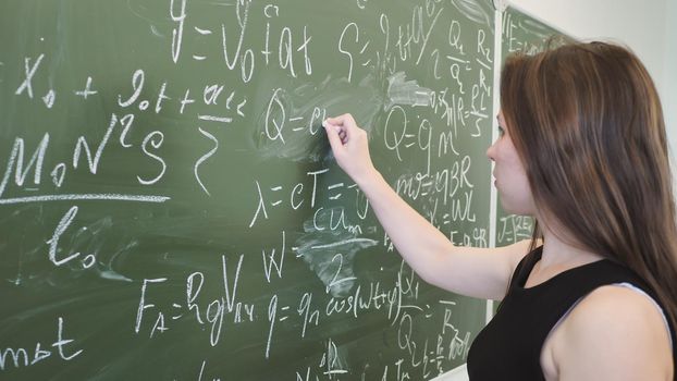 Girl schoolgirl writes on the blackboard a mathematical formula and poses in front of a video camera