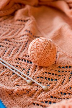 A ball of yarn and a pair of wooden needles lying on the orange knitted plaid