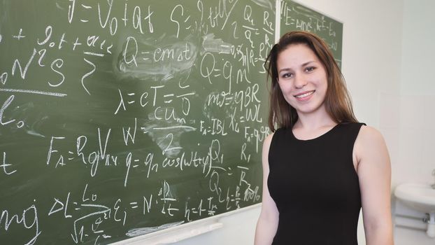 Girl schoolgirl posing on the blackboard a mathematical formula and poses in front of a video camera