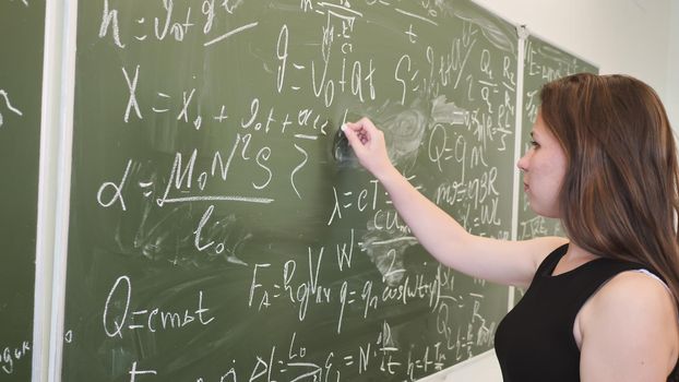 Girl schoolgirl writes on the blackboard a mathematical formula and poses in front of a video camera