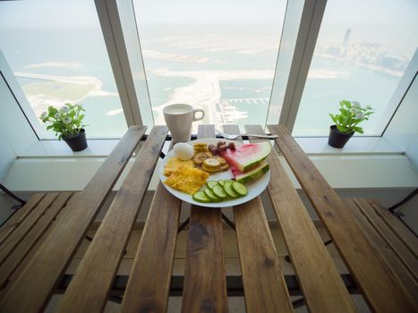 Light breakfast with scrambled eggs and fruit on the background of a skyscraper window on Palm Jumeirah. Dubai.