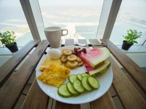 Light breakfast with scrambled eggs and fruit on the background of a skyscraper window on Palm Jumeirah. Dubai.