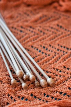 Many light knit knitting needles lie on a bright orange plaid.