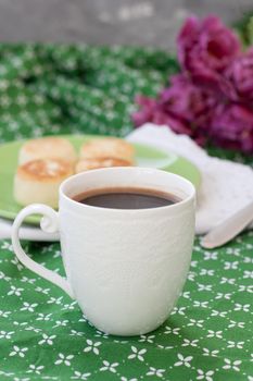 Black coffee in a white sophisticated cup, delicious dietary cheesecakes from home-made farmer cheese for breakfast, a bouquet of purple tulips on a green tablecloth.