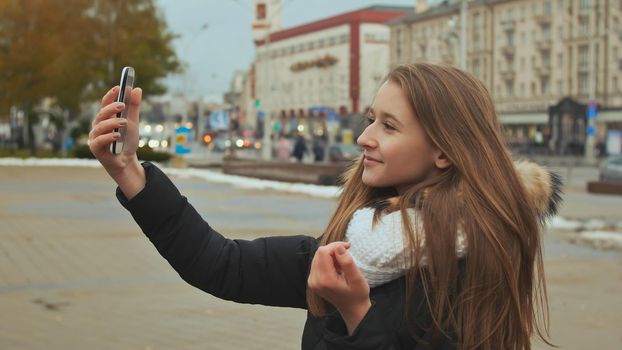 Young beautiful girl in jacket does selfi autumn in one of the city streets.