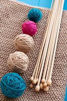 Colorful balls and wooden needles lying on beige knitted background