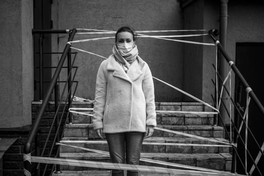 Photo of a girl in a mask. Standing on the street with danger warning tapes.