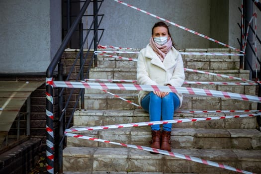 Photo of a girl in a mask. Sitting on the street with danger warning tapes.