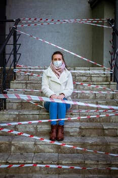 Photo of a girl in a mask. Sitting on the street with danger warning tapes.