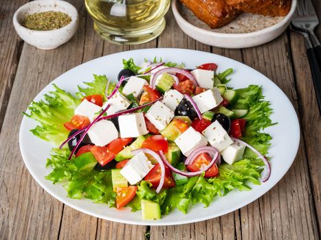 Greek salad on white plate on old rustic wooden table, side view
