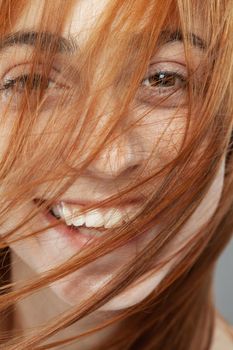 Beautiful dark burnt orange windy hair girl smiling. Studio portrait with happy face expression against gray background...