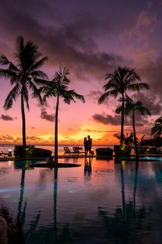 couple men and woman watching sunset on a tropical beach in Mauritius with palm trees by the swimming pool, Tropical sunset on the beach in Mauritius