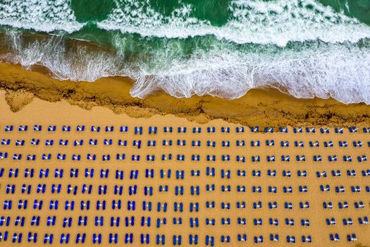 Aerial view of an amazing beach with, blue lounge chairs, with umbrellas, and turquoise sea.