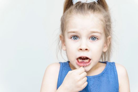 Cute scared girl pulling her loose tooth using a string