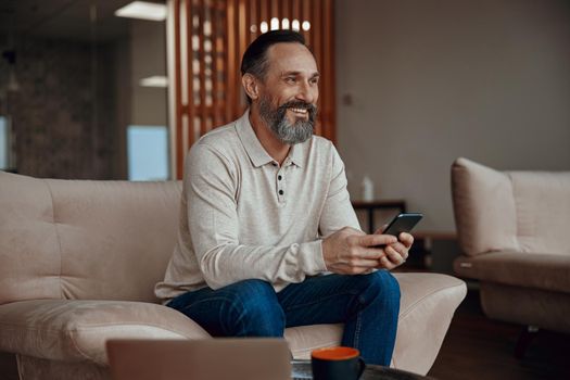 Smiling man sitting in armchair and holding smartphone