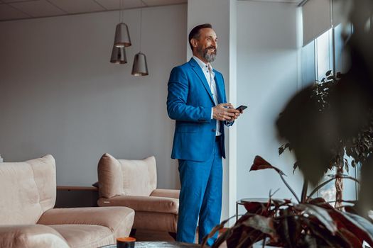 Smiling bearded man with smartphone standing in modern office space