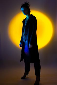 a woman in a black leather coat, in high-heeled shoes illuminated by colored light