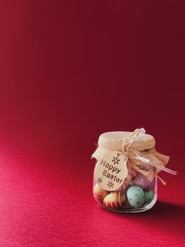 Happy Easter. Colourful painted easter eggs in glass jar on red background, Christian religion and holiday