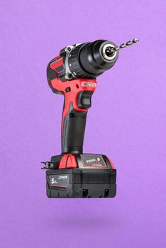 Cordless drill in black and red. Screwdriver with a drill on a purple background. Modern carpentry cordless tool close-up.