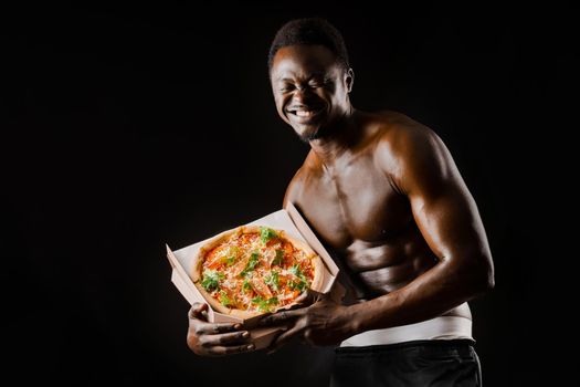 Funny black man with pizza smiles. Undressed african works in safety food delivery. Fit man with food from restaurand. Black naked man.