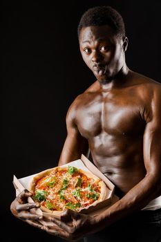 Surprised black fit man with pizza in hands. Tasty food delivery. African with athletic body shows a pizza. Sexy man with tasty pizza from restaurant.