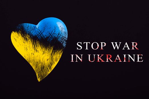 Stop war in Ukraine. Save Ukraine. The heart is painted in the colors of the Ukrainian flag - blue and yellow. Stop war text, poster on black background