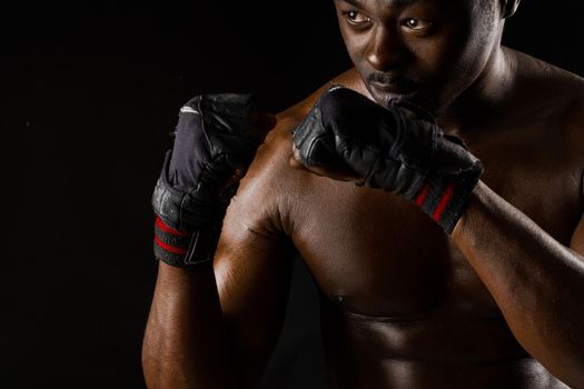 Athletic african fighter on black background. Dark skinned undressed man shows a fight. Advert for sport club and gym. Professional boxing and karate.