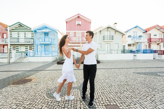Young couple stays in tango pose and looks each others in Aveiro, Portugal near colourful and peaceful houses. Lifestyle. Having fun,