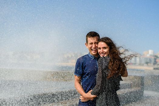 Splashing a wave of the ocean on two people in love. Lifestyle of couple. Having fun and laughs. Porto, Portugal, near Atlantic ocean