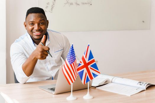 English and British flags in front. Black handsome translator uses his laptop for online work according social distancing