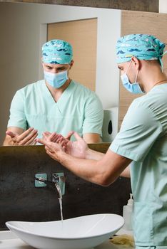 Surgeon looks at the cleanliness of his hands after washing under a stream of water. Wash your hands under running water