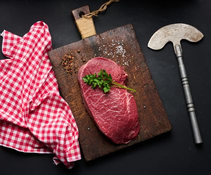 Raw beef tenderloin lies on a cutting board and spices for cooking on a black table