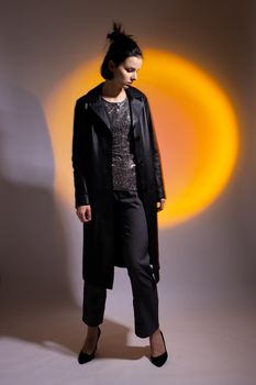 a woman in a black leather coat, in high-heeled shoes illuminated by colored light