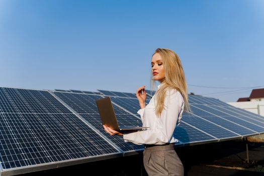 Investor and solar panels. Blonde woman with laptop near blue solar panels row on ground. electricity for home. Sustainability of planet. Green energy