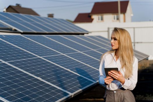 Investor woman stand with tablet near blue solar panels row on the ground. Free electricity for home. Sustainability of planet. Green energy