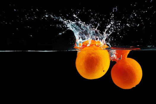 Oranges falling into water against black background, studio shot