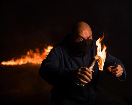 A masked man is holding a burning bottle. Molotov cocktail.
