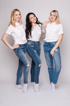 Three beautiful women in white shirts and jeans posing