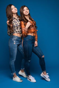 Two slim sisters in checkered shirts and jeans posing