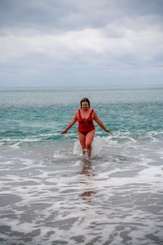 Woman in a bathing suit at the sea. A fat young woman in a red swimsuit enters the water during the surf