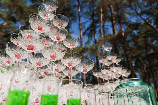 Drink coctkail catering for wedding. Big pyramid of glasses with champagne and red cherry inside on business meeting at summer day in the forest