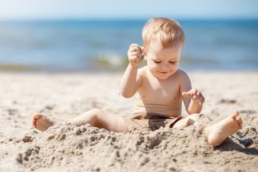 A happy little boy plays with sand in the beach