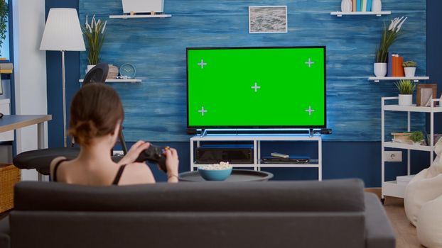 Gamer girl playing console video games with wireless controller on green screen tv relaxing on couch