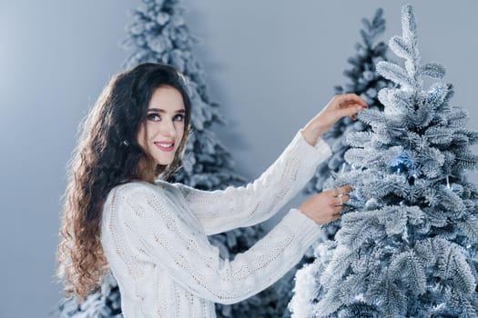 Attractive girl with christmas tree. Young woman touches christmas tree. Winter holidays celebration.