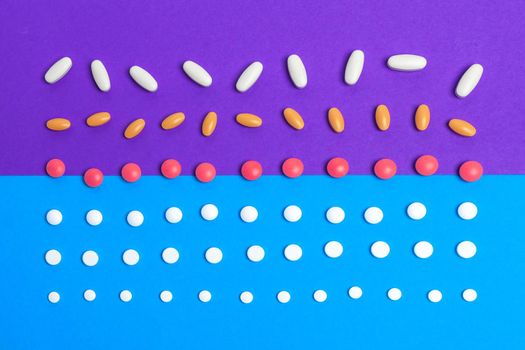 A pile of multicolored pills on blue background. Top view.