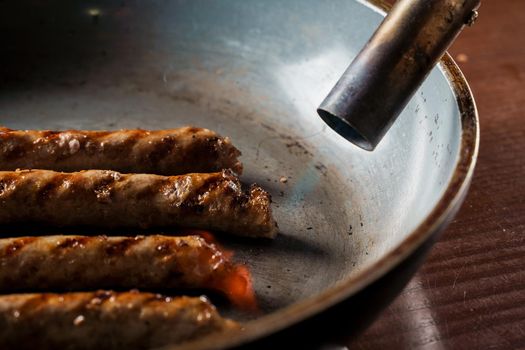 Grilled sausages in a frying pan are fired with a gas burner.