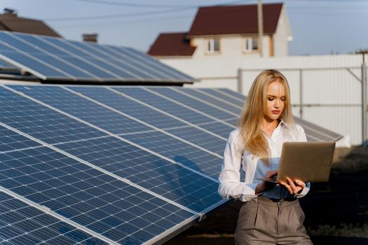 Investor woman stand with laptop near blue solar panels row on the ground. Free electricity for home. Sustainability of planet. Green energy