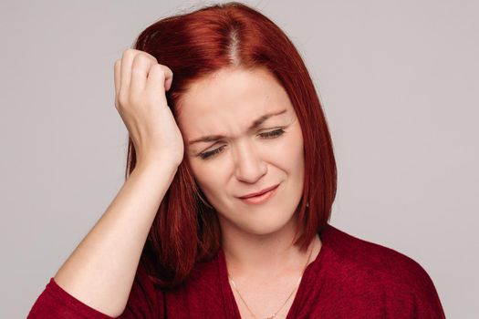 Clouse up of pretty red haired woman in bordo blouse with headache.