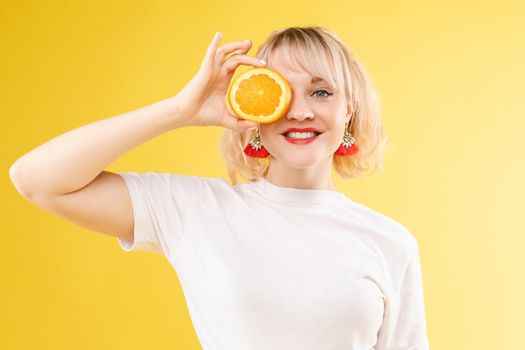 A woman with oranges in her eyes. Red lipstick lips. Merry, cheerful girl exudes positive, spoiled oranges. Isolated on yellow background