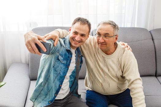 Smiling father and adult son photographing together at home.